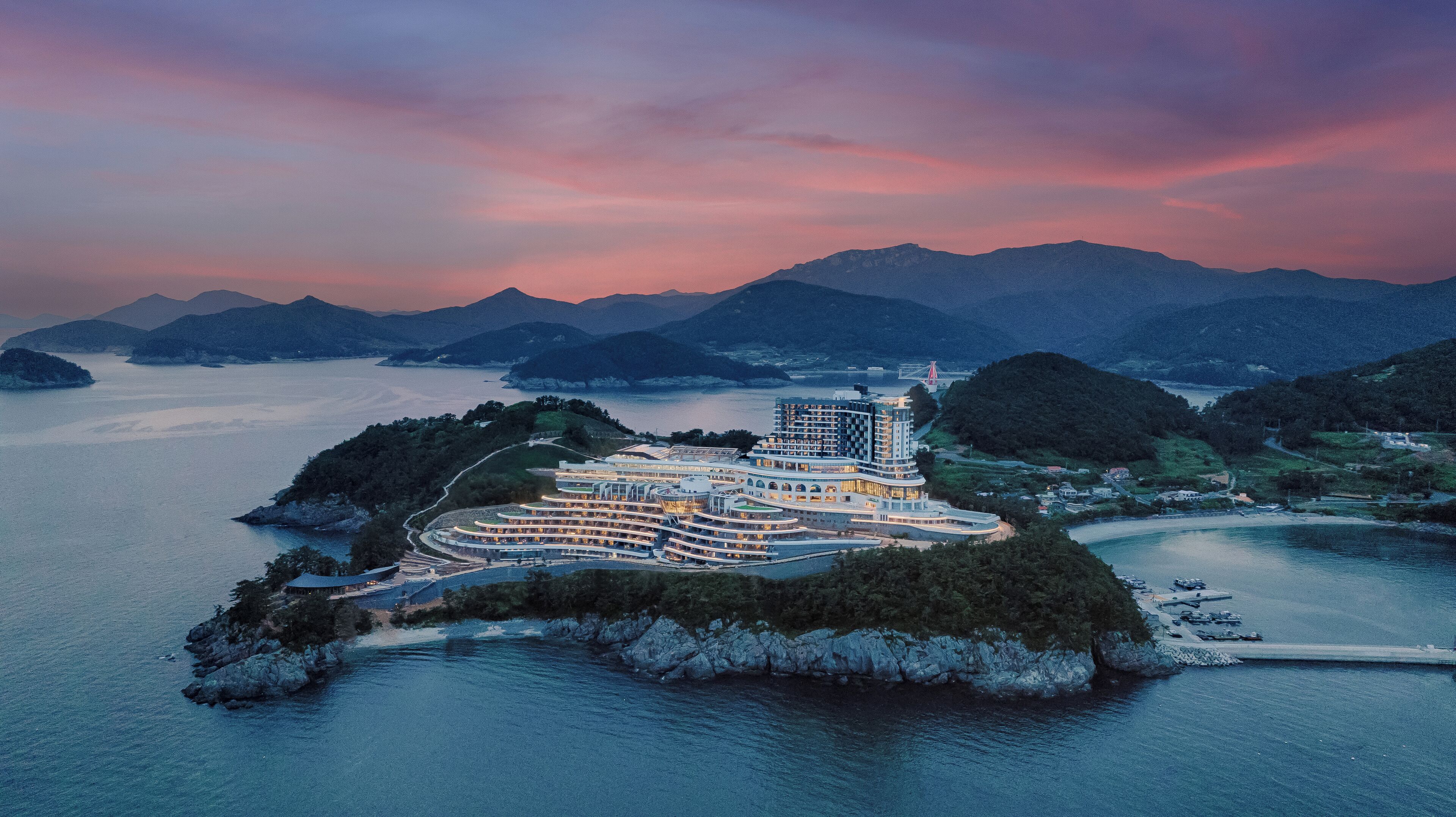 Un hotel frente al agua con varias edificaciones, un puente y montañas circundantes.