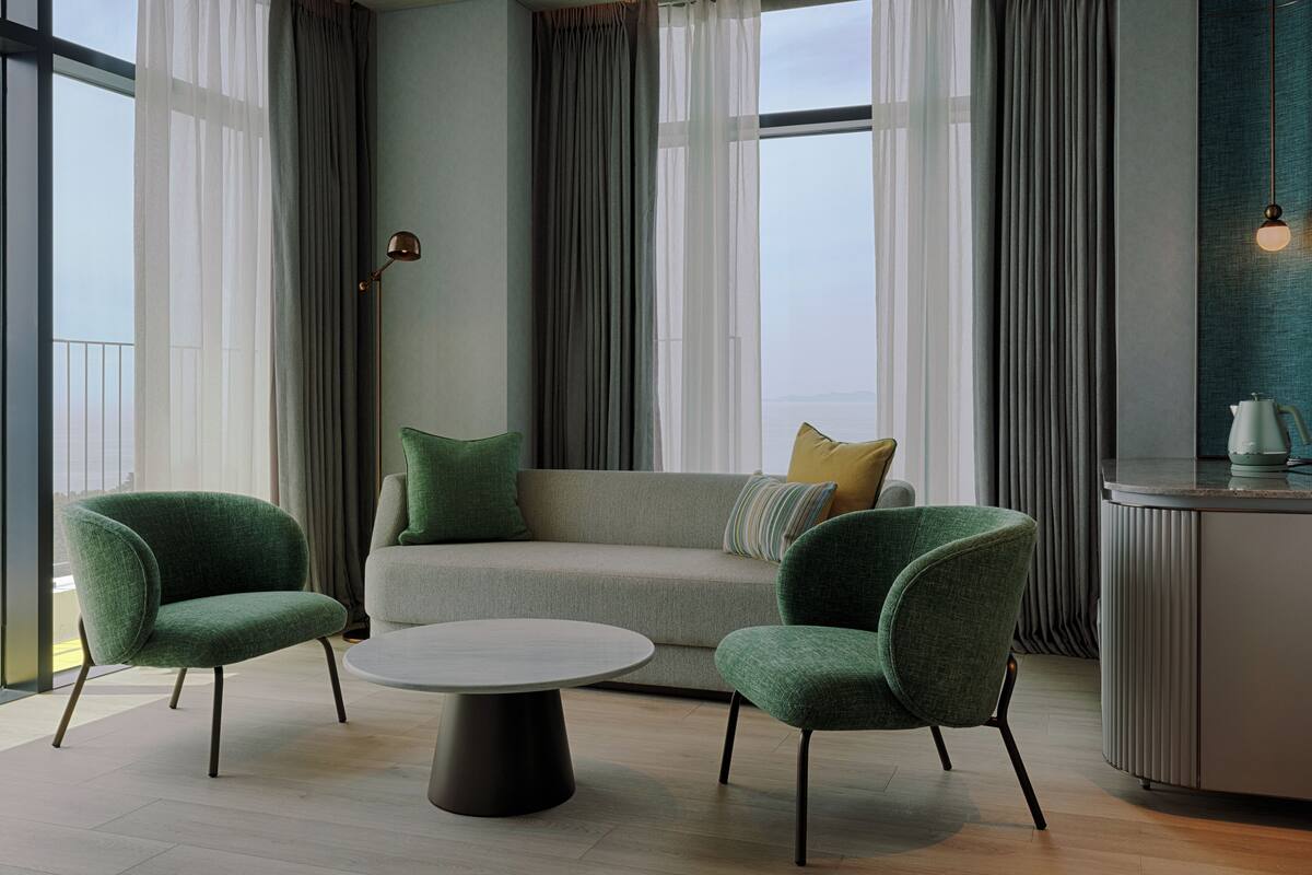 A modern living room with a sofa, two armchairs, a coffee table, and a view of the city through large windows.