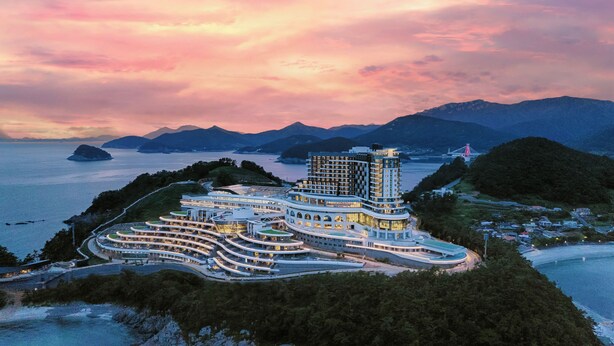 Un hôtel moderne à l’architecture originale, caractérisée par des lignes courbes, situé sur une île côtière et offrant une vue sur la mer et les montagnes.