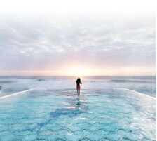 Una persona está de pie en una piscina infinita de fondo de cristal con vista al océano y un atardecer de fondo.
