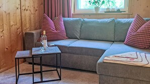 A cozy living room with a grey sofa, two patterned pillows, a small coffee table, and a window with a view of greenery.