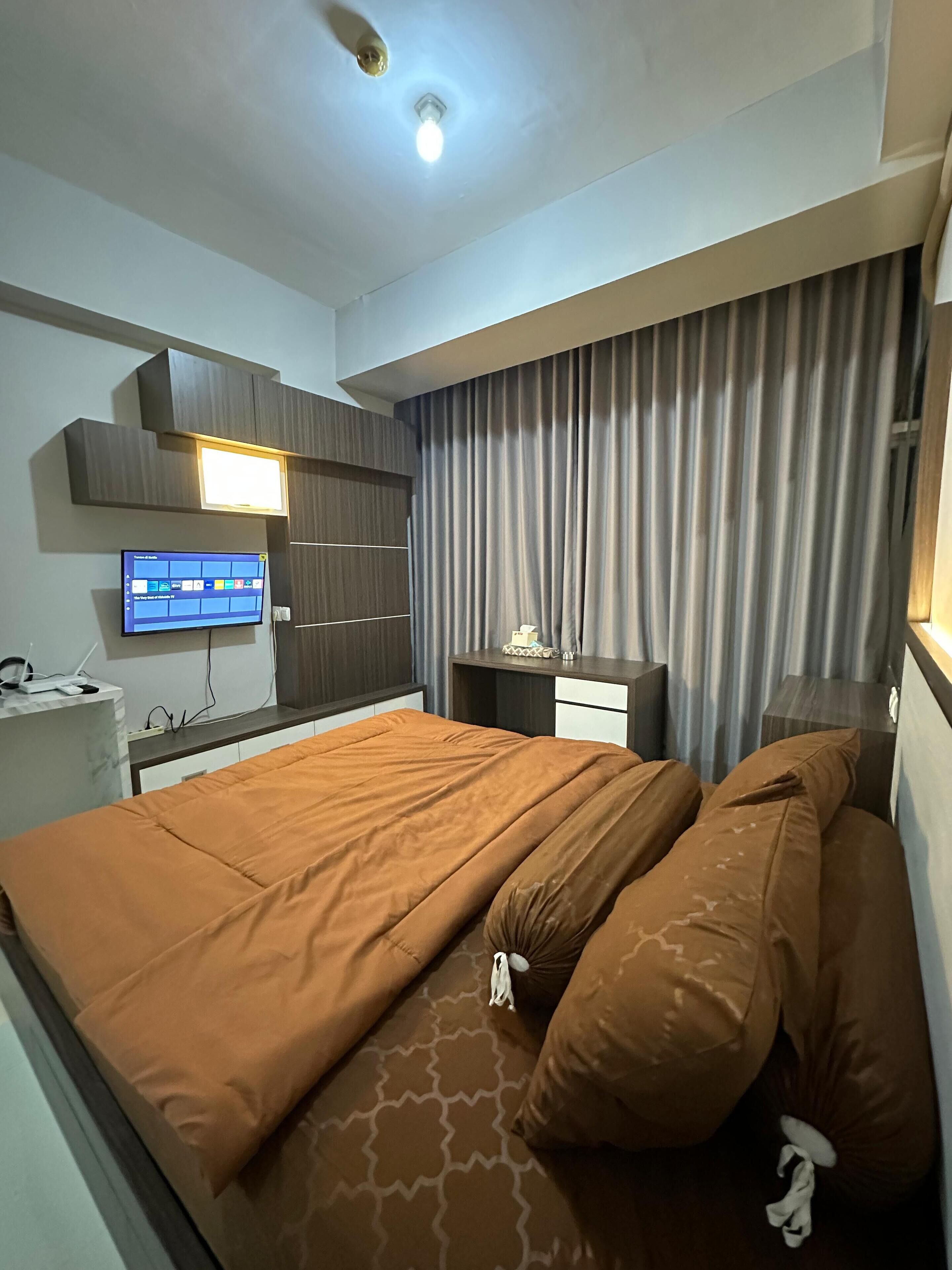Una habitación de hotel con cama, escritorio, televisor y cortina.