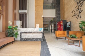 A modern lobby with a marble reception desk, wooden accents, and orange seating. - ROKET ROOM Majestic By Reccoma (Gading Serpong)