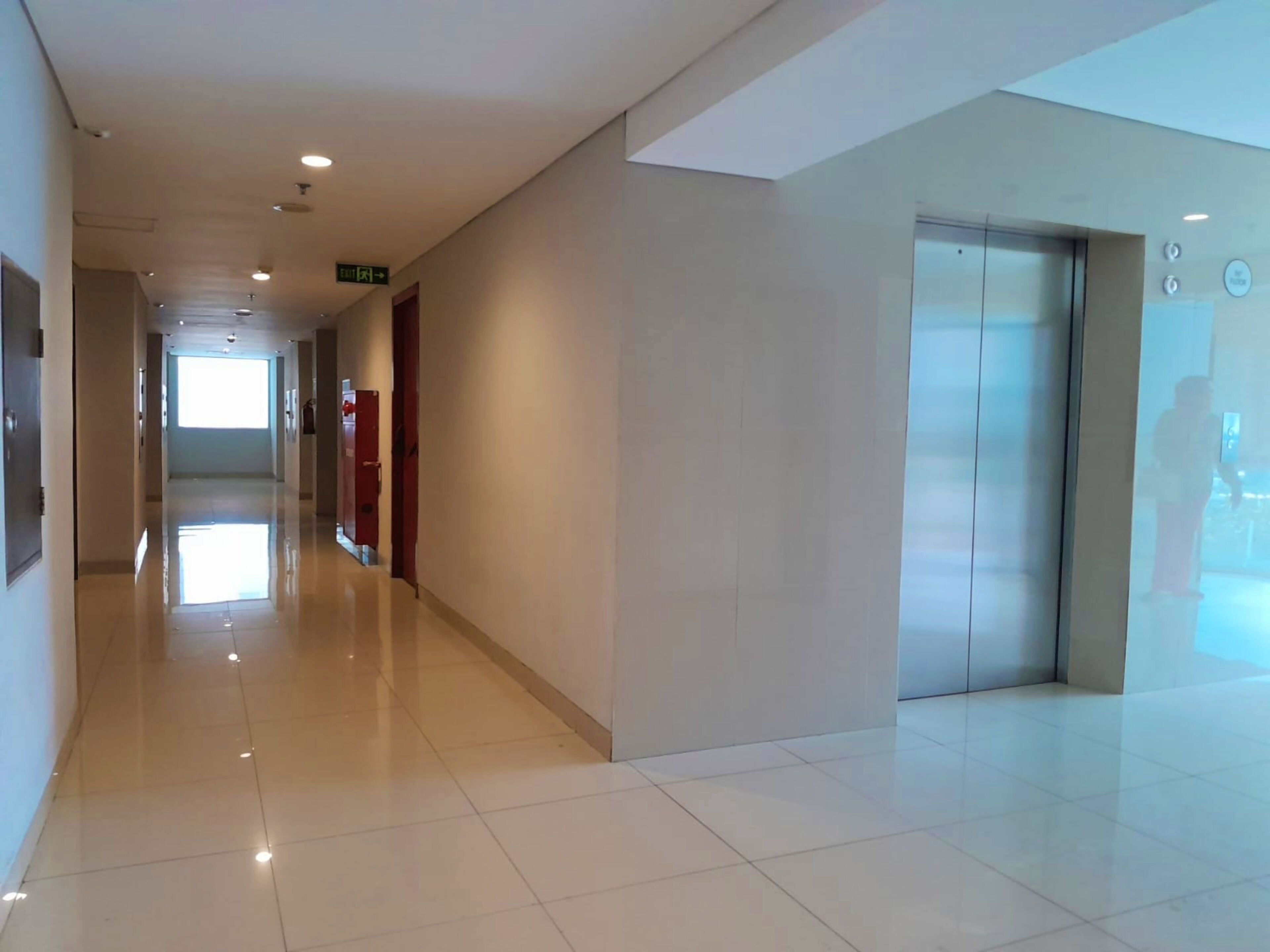 A clean, modern hallway with a shiny tiled floor, a red door, and an elevator.