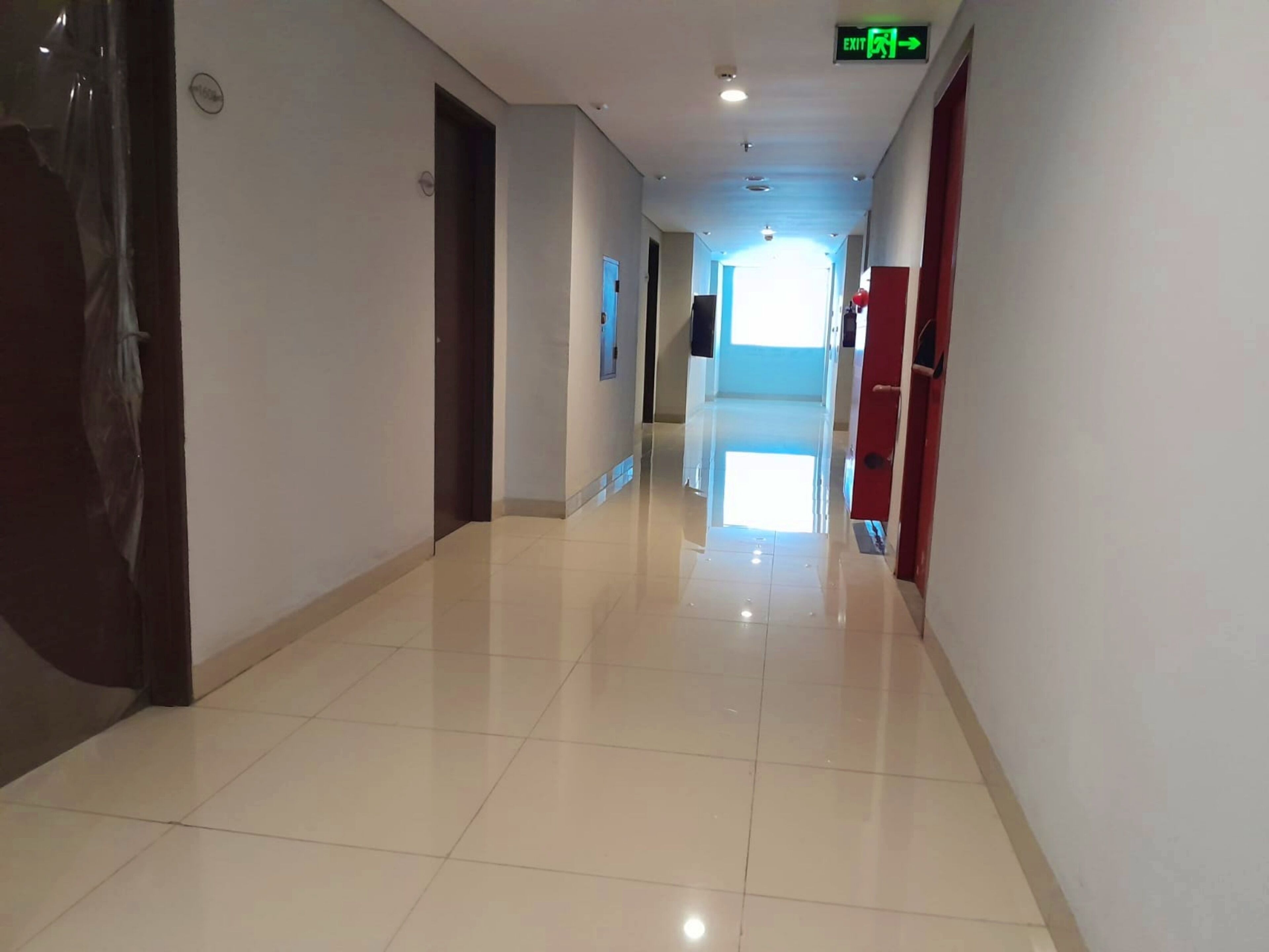 A clean, well-lit hallway with a shiny tiled floor, a visible exit sign, and a door on the left.