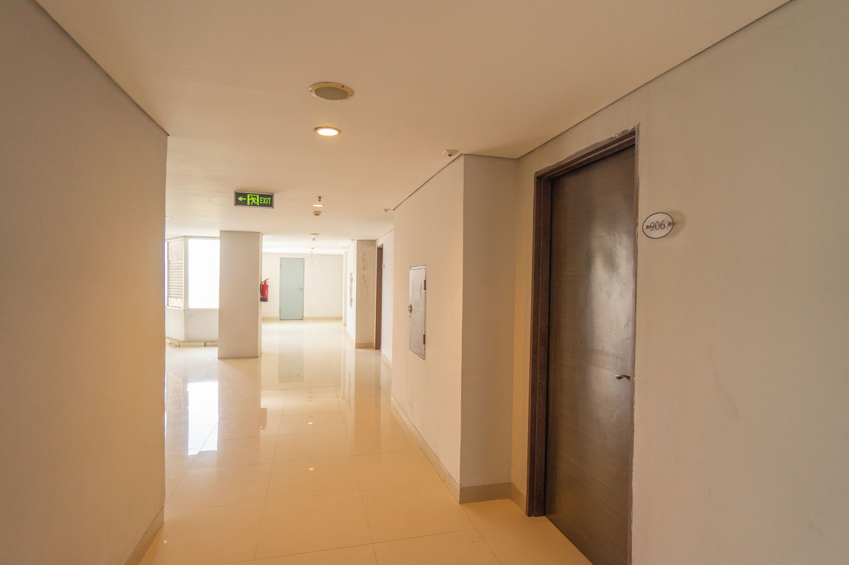 A clean, well-lit hallway with a polished floor, a door with a number plate, and an exit sign.