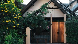 A house with a wooden gate, a bench, and a garden with yellow flowers.