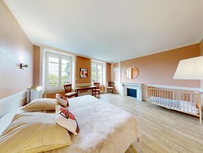Une chambre à coucher avec un lit, un berceau, une cheminée, un bureau et de grandes fenêtres.