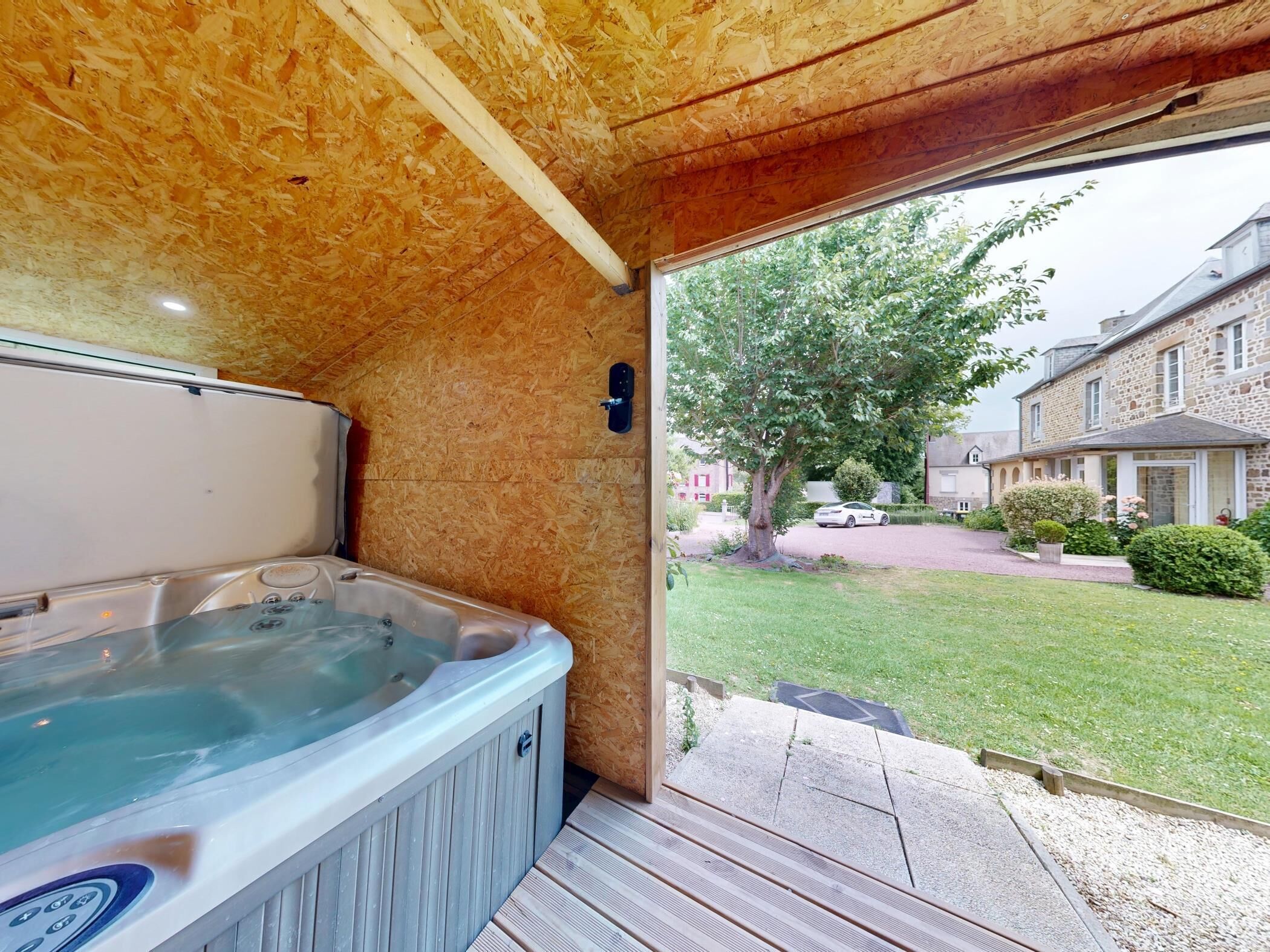Un bain à remous dans une pièce en bois, avec vue sur une maison et un jardin.