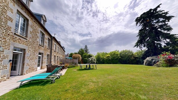 A stone building with a grassy yard, a pool, and a large tree.