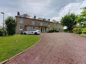 Un bâtiment en pierre avec une allée en gravier et une voiture garée.
