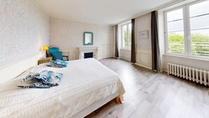 A bedroom with a bed, a chair, a fireplace, and a large window.