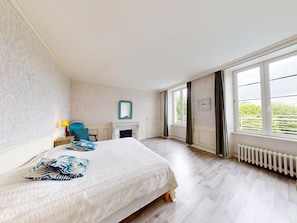 A spacious bedroom with a large bed, a fireplace, and a view of greenery through the windows. - Clos Minotte 30 pers 2 Cottage : jacuzzi, billards, baby-foot (Tessy-Bocage)