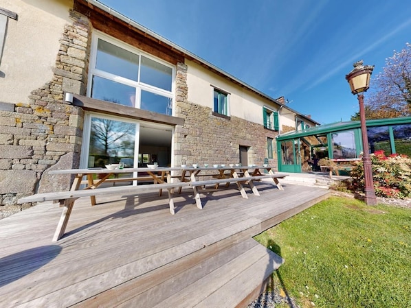 A building with stone walls, large windows, and a wooden deck with picnic tables.