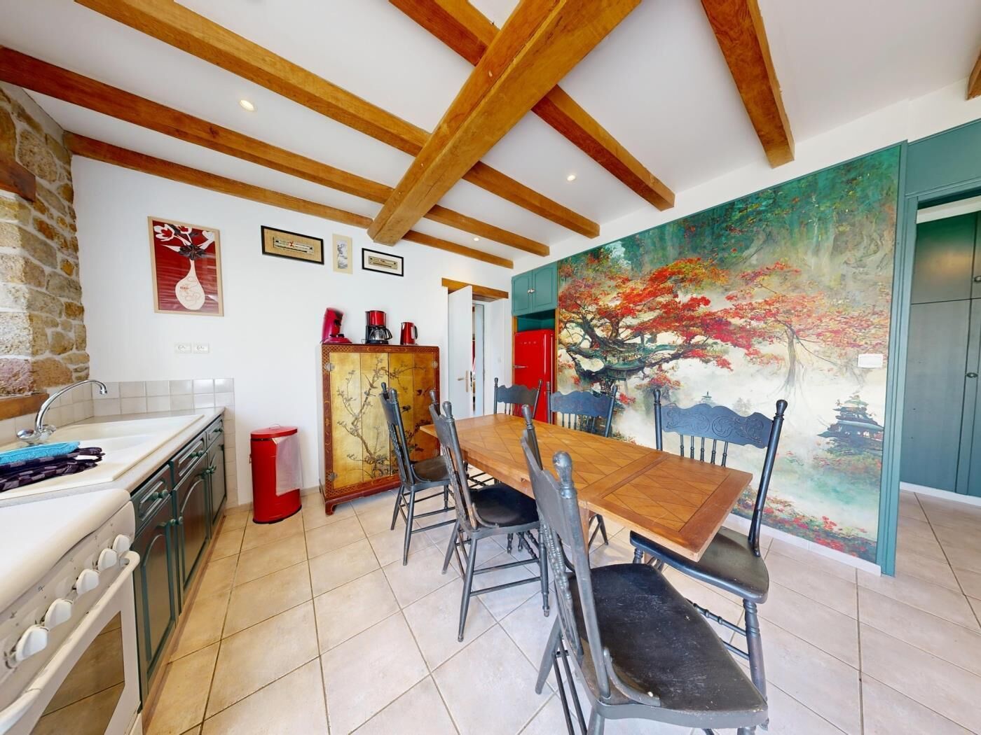 A dining area with a wooden table and chairs, a kitchen with a stove, and a mural on the wall.