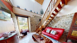 Una sala de estar con sofá rojo, escalera de madera, paredes de piedra y vistas a través de un ventanal.