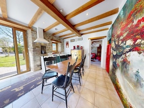 A spacious dining area with a large wooden table and chairs, a stone wall, and a view of the outdoors.