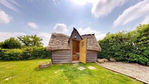 A small wooden cabin with a thatched roof, a wooden door, and a small porch. - La Longère 1750 30pers Hambye, piscine grand jardin (Hambye)