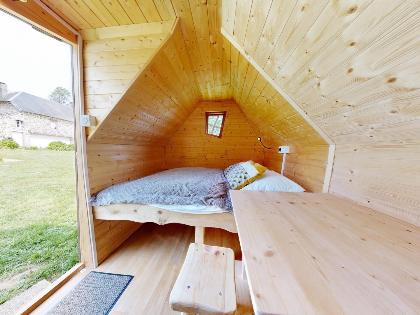 A wooden loft bedroom with a bed, a small window, and a wooden table.