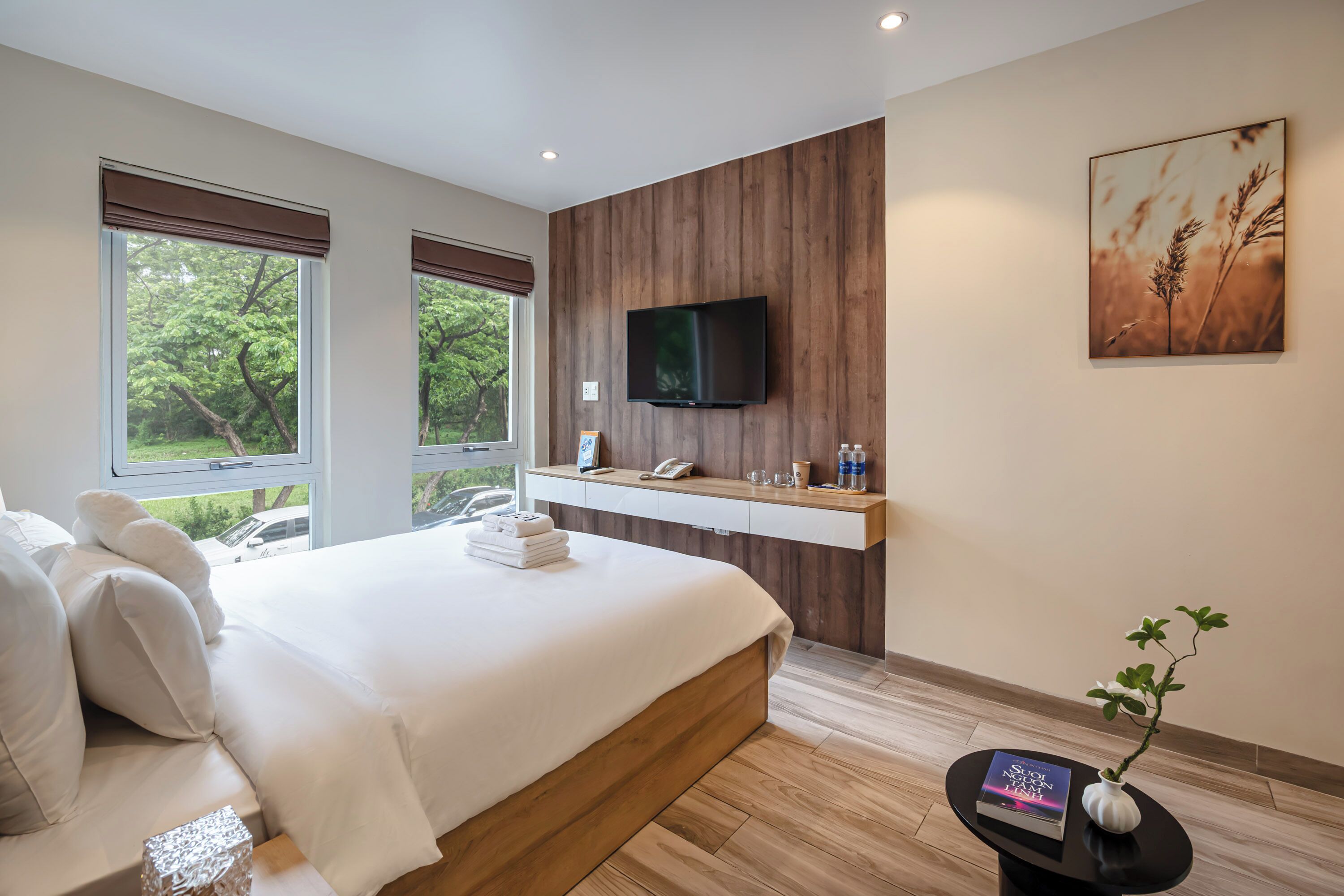 A modern bedroom with a large bed, a mounted TV, and a view of greenery outside.