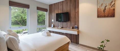 A modern bedroom with a large bed, a mounted TV, and a view of greenery outside.