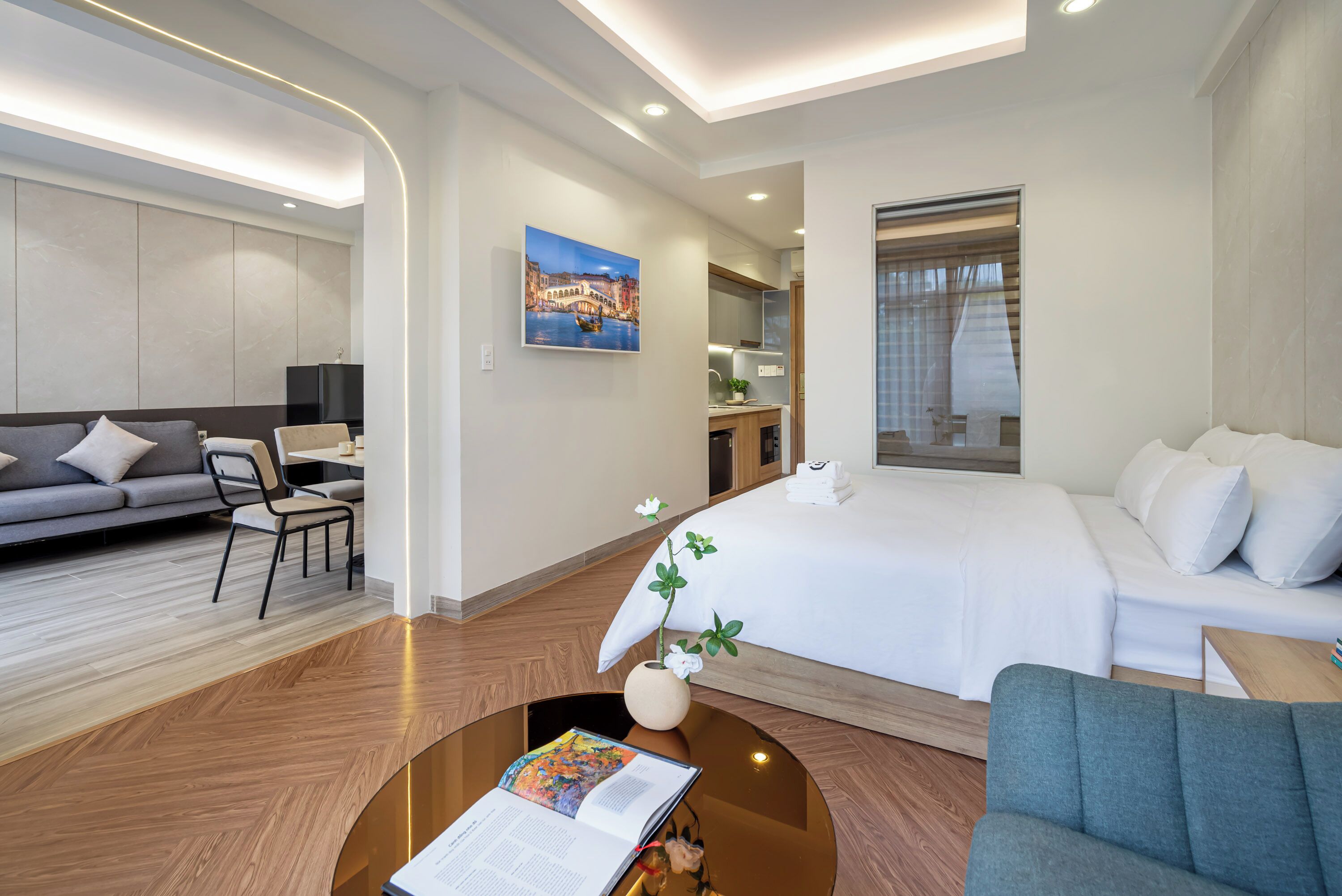 A modern hotel room with a large bed, a sofa, a dining area, and a view of the city.