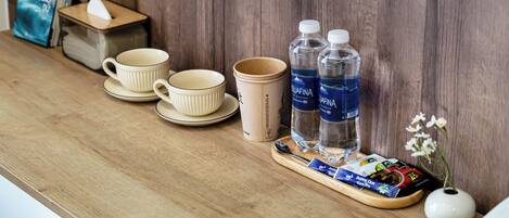 A wooden counter with a tissue box, two cups, two water bottles, a tray with coffee packets, and a small vase with flowers.