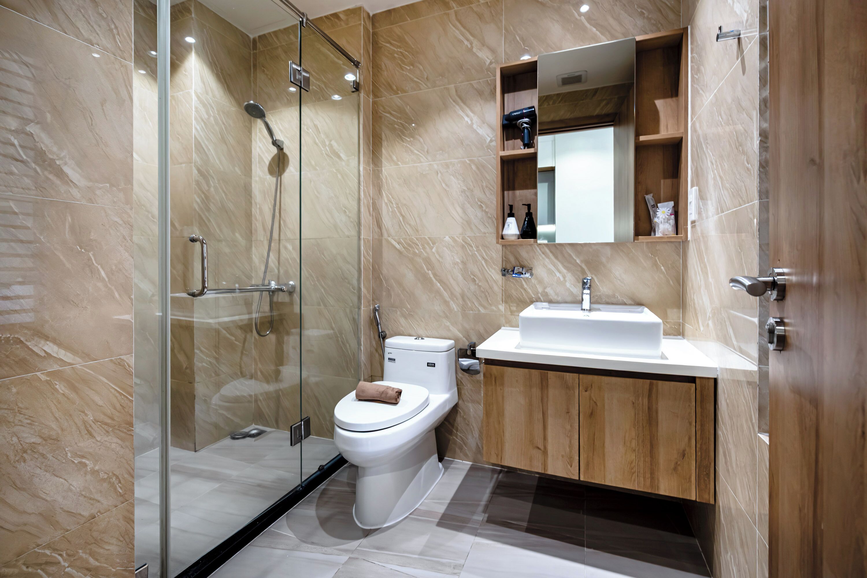 A modern bathroom with a glass-enclosed shower, a toilet, and a wooden vanity with a mirror.