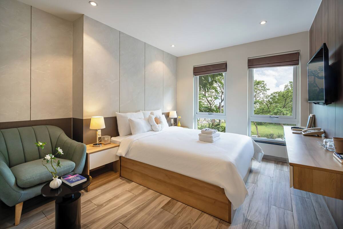 A modern hotel room with a large bed, a desk, a chair, and a TV.