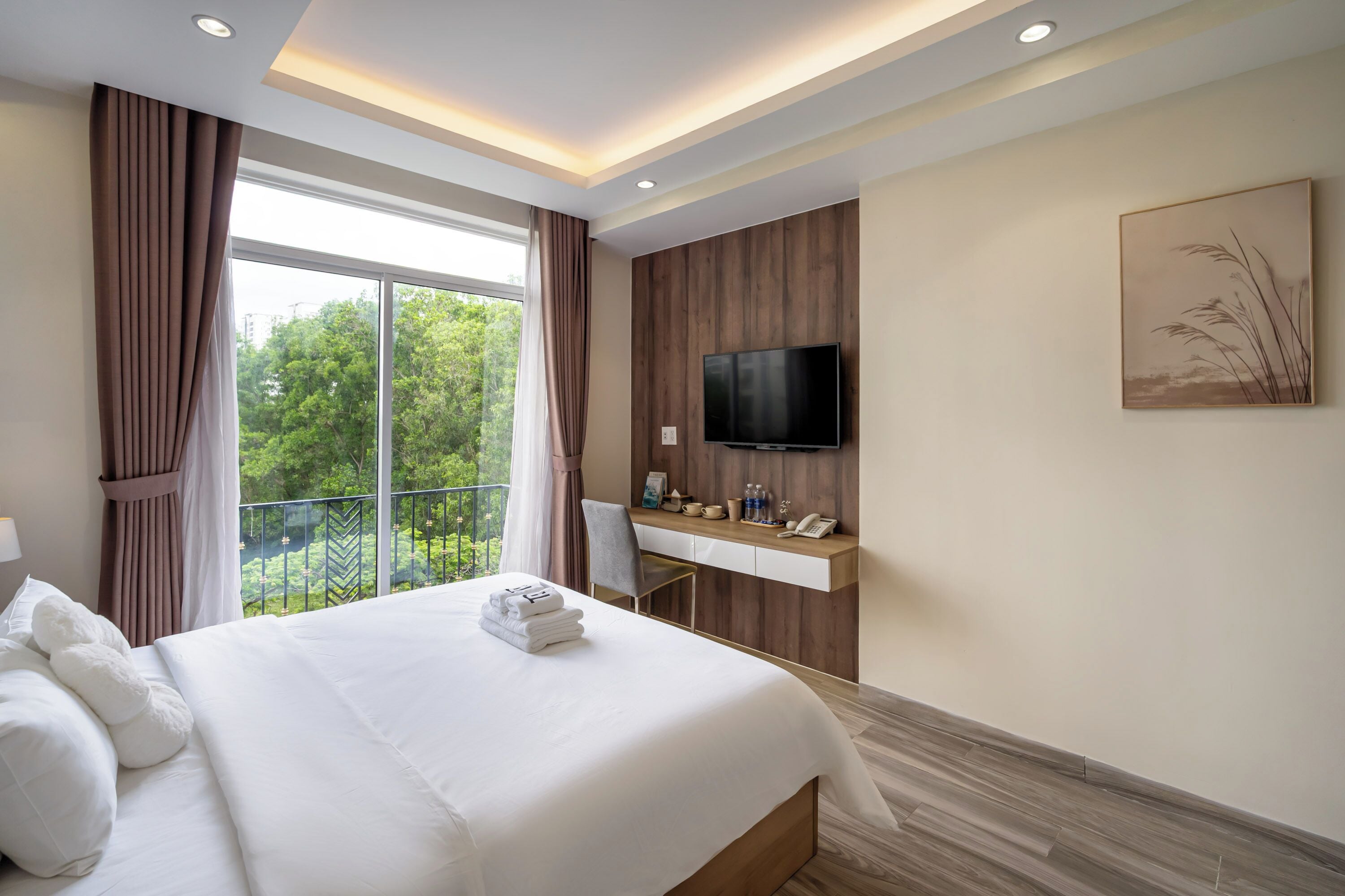 Ein modernes Hotelzimmer mit einem großen Bett, einem Schreibtisch, einem Flachbildfernseher und einem Balkon mit Blick auf Bäume.