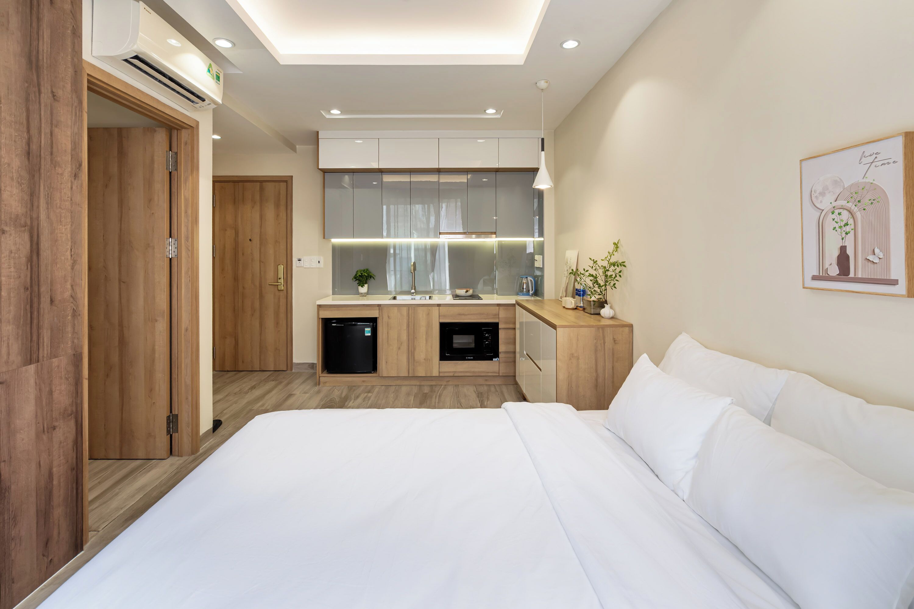 Ett modernt hotellrum med en stor säng, ett träskåp, ett inbyggt kök med mikrovågsugn och en liten matplats.