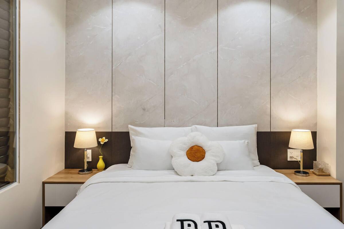 A hotel room with a large bed, two bedside tables with lamps, a wall with a textured panel, and a window with blinds.