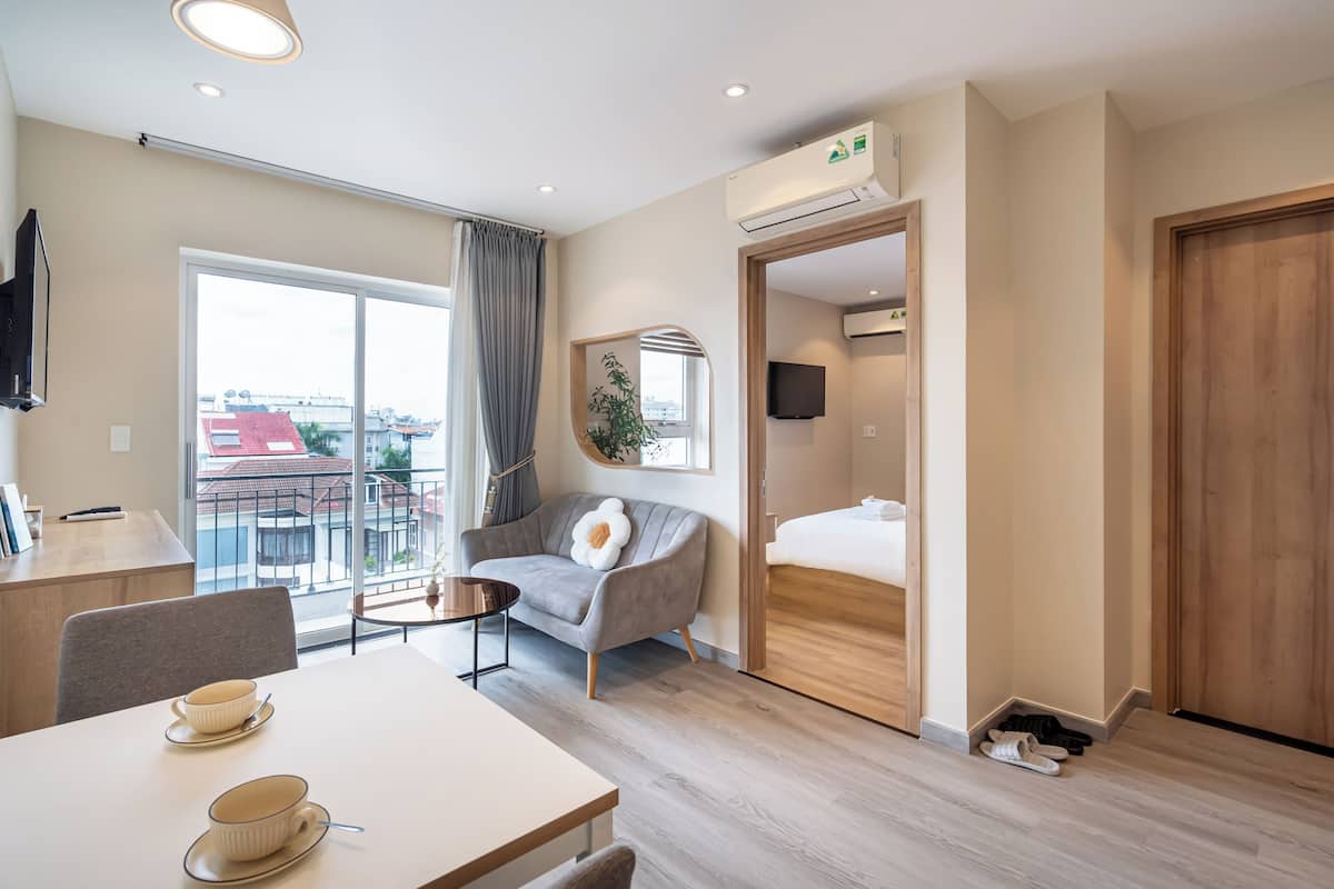 A modern hotel room with a dining area, a sofa, a bed, and a balcony with a view of buildings.