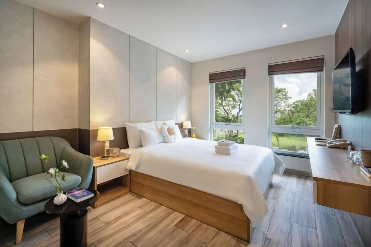 A modern hotel room with a large bed, a desk, a chair, and a TV.
