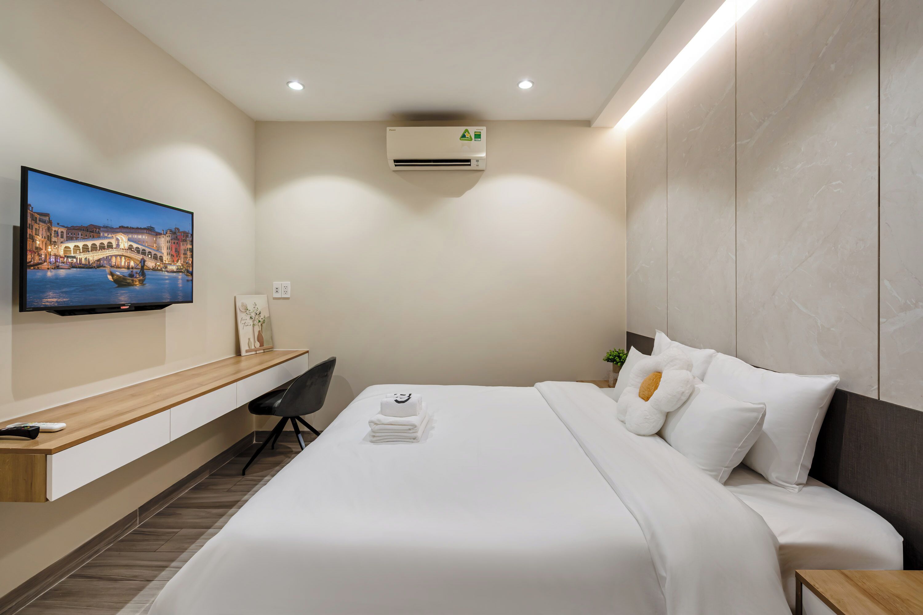 A modern hotel room with a bed, a desk, a flat-screen TV, and an air conditioning unit.