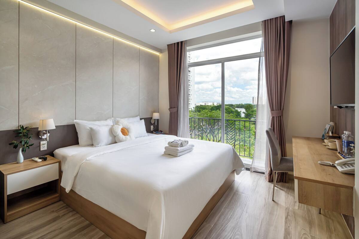 A modern hotel room with a large bed, a desk, and a balcony with a view.
