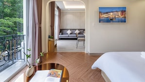Ein modernes Hotelzimmer mit einem großen Bett, einer Couch, einem Esstisch und Blick auf eine Stadtlandschaft durch ein Fenster.