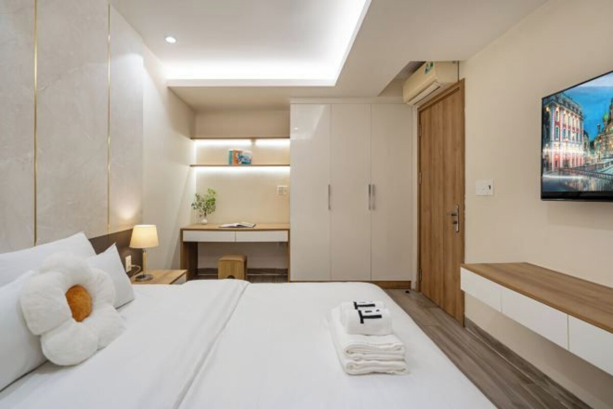A modern hotel room with a neatly made bed, a desk with a lamp, a TV on the wall, and a wooden cabinet.