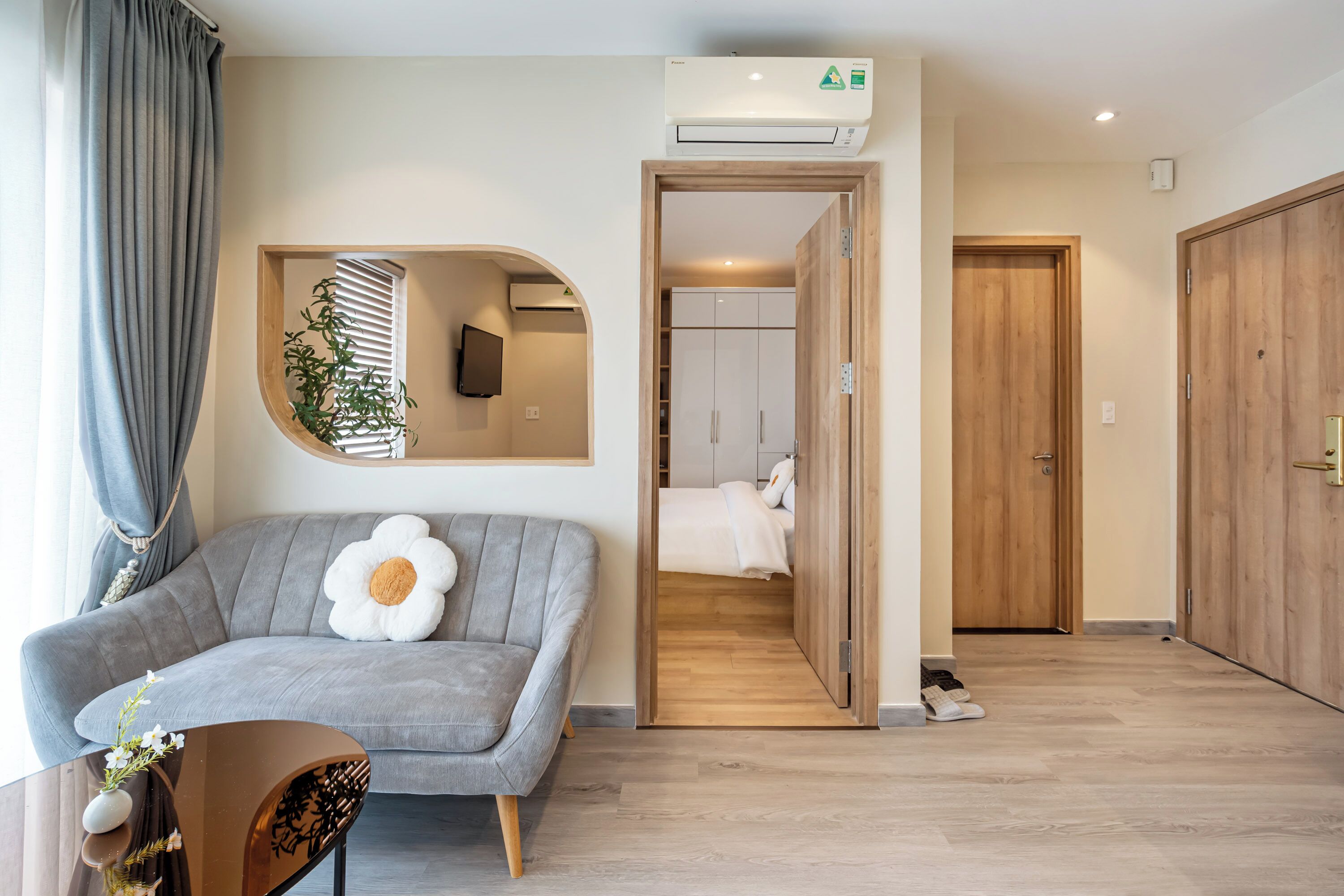 Ein modernes Hotelzimmer mit grauem Sofa, einem großen Spiegel und einem Holzschrank.