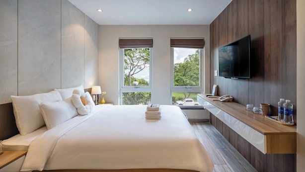 Ein modernes Hotelzimmer mit einem großen Bett, einem an der Wand montierten Fernseher und einem Fenster mit Blick auf Bäume.