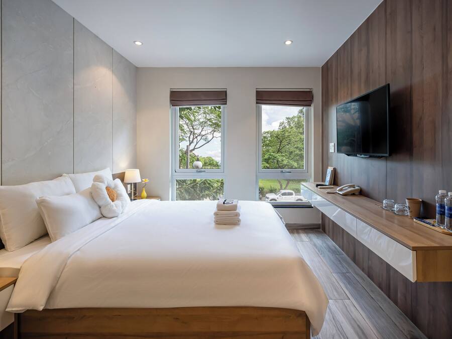 Una habitación de hotel moderna con una cama grande, un televisor montado en la pared y una ventana con vista a árboles.
