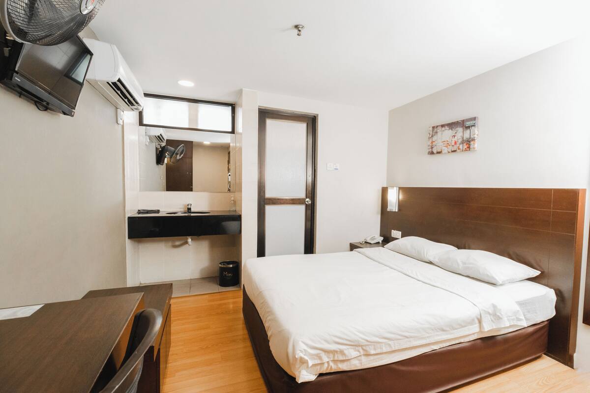A hotel room with a bed, bedside table, desk, and a mirror.