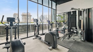 A gym with various exercise equipment, large windows, and a view of the cityscape. - Sano by Kozystay - Sudirman (Jakarta)