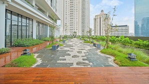 A modern urban courtyard with a wooden deck, stone pathway, and lush greenery. - Sano by Kozystay - Sudirman (Jakarta)