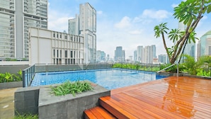 A rooftop pool with a wooden deck, surrounded by greenery and city buildings. - Sano by Kozystay - Sudirman (Jakarta)