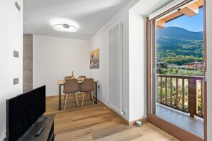 Habitación moderna con televisión, mesa de comedor, sillas y vista a un paisaje montañoso desde un balcón.