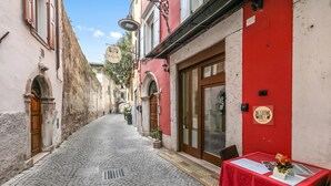 Une ruelle pavée étroite, bordée d’un immeuble rouge qui se distingue par sa grande porte en bois et son panneau indicateur.