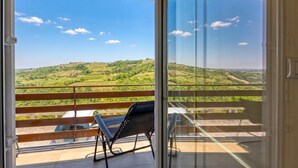 A balcony with a view of green hills, a chair, and a car parked outside. - Neda Apartment: Terrace Views Goriška Brda, Dobrovo v Brdih, Slovenia (Dobrovo v Brdih)