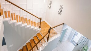 Un interior moderno con una escalera de madera, paredes blancas y vista a una habitación con una planta.