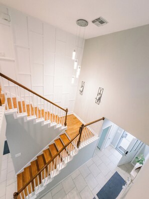 Un interno moderno con una scala in legno, pareti bianche e vista su una stanza con una pianta.